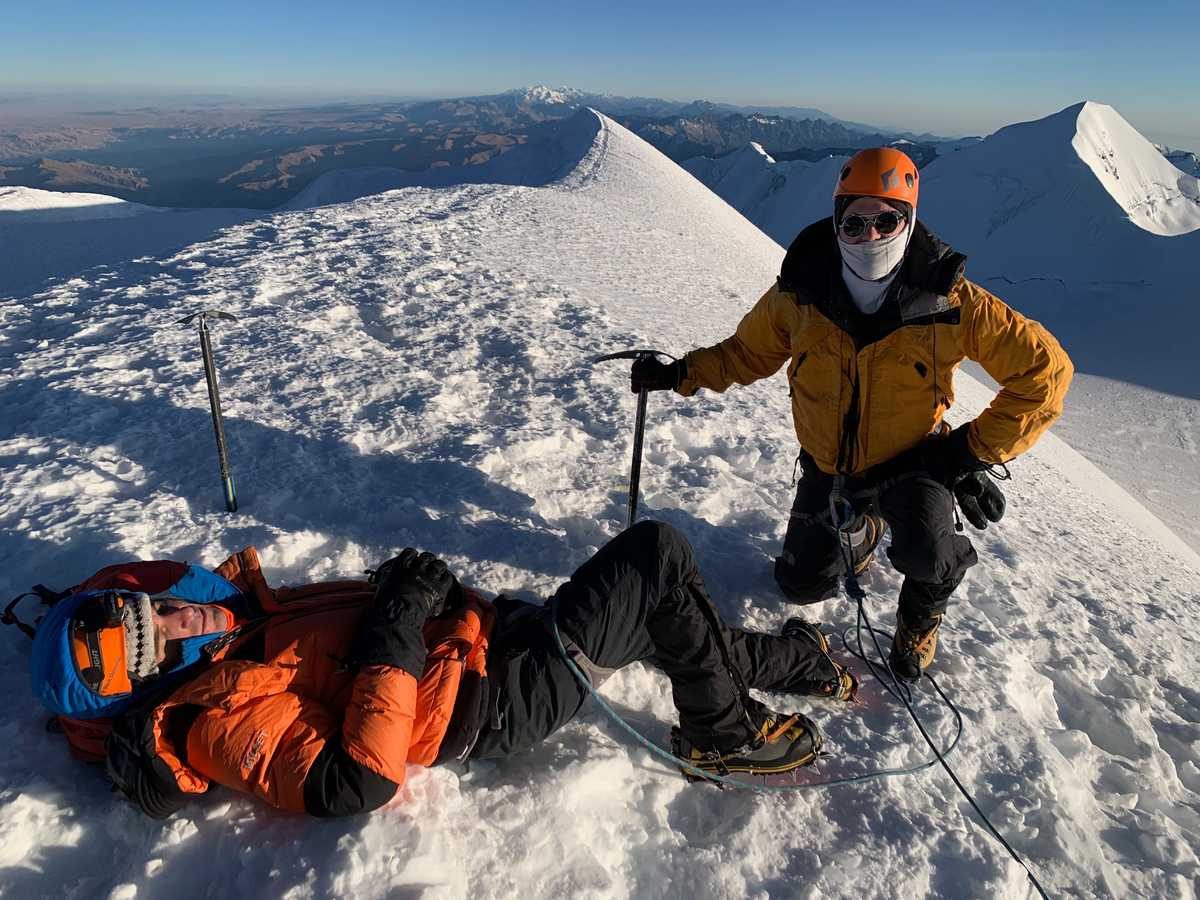 Two men on the summit of Illimani. One is sleeping and the other is posing with an ice axe.